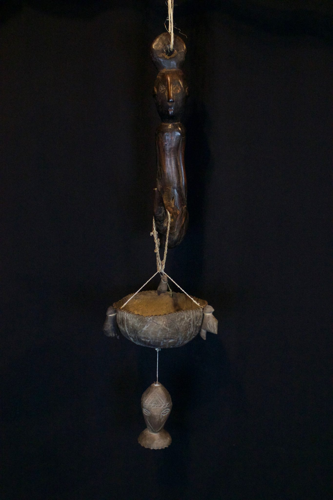 Hanging Effigy and Herb Bowl - set, East Sumba Island, Indonesia, Soru village, Early 20th c, Wood, coconut, fiber string. The effigy hanger gives great healing power to the herbs placed in the coconut bowl suspended below it. The bowl has three bird figure and three carved faces with an amulet head hanging below it. 30” x 6” x 6”, $1200.
